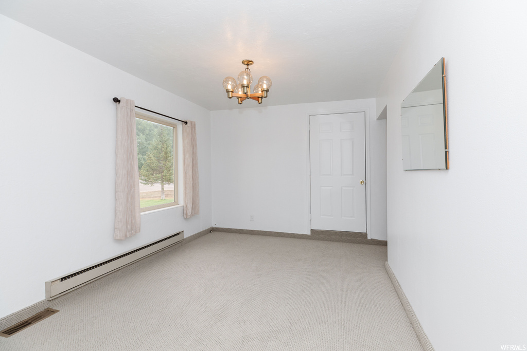 Spare room with a baseboard radiator, light carpet, and a notable chandelier