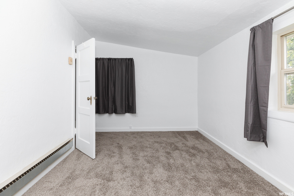 Empty room featuring lofted ceiling, light carpet, and baseboard heating