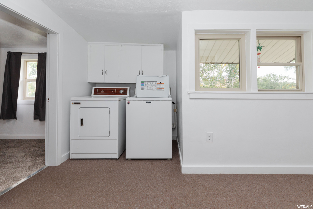 Clothes washing area with light colored carpet, cabinets, and washer and dryer