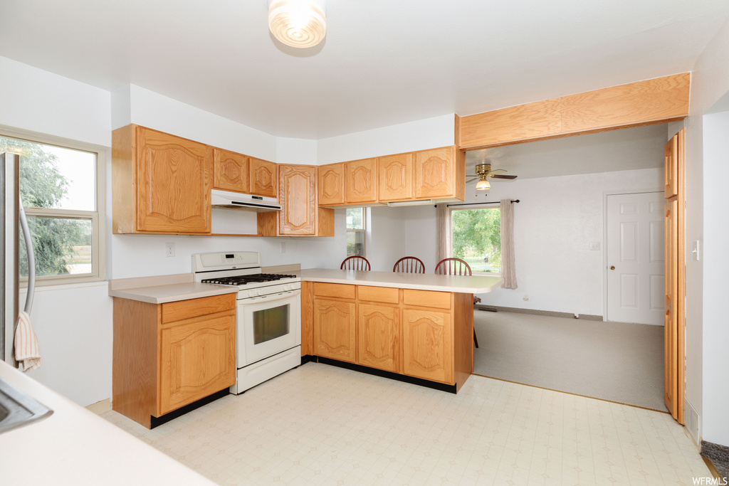 Kitchen featuring kitchen peninsula, white gas range oven, ceiling fan, stainless steel fridge, and light tile flooring