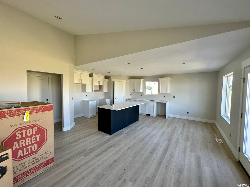 Kitchen featuring a kitchen island, vaulted ceiling high, countertops light, white cabinetry, and light hardwood flooring