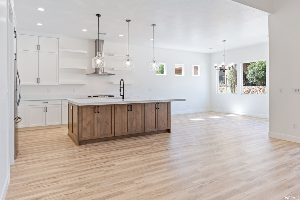 Kitchen with a center island with sink, white cabinets, and light hardwood floors