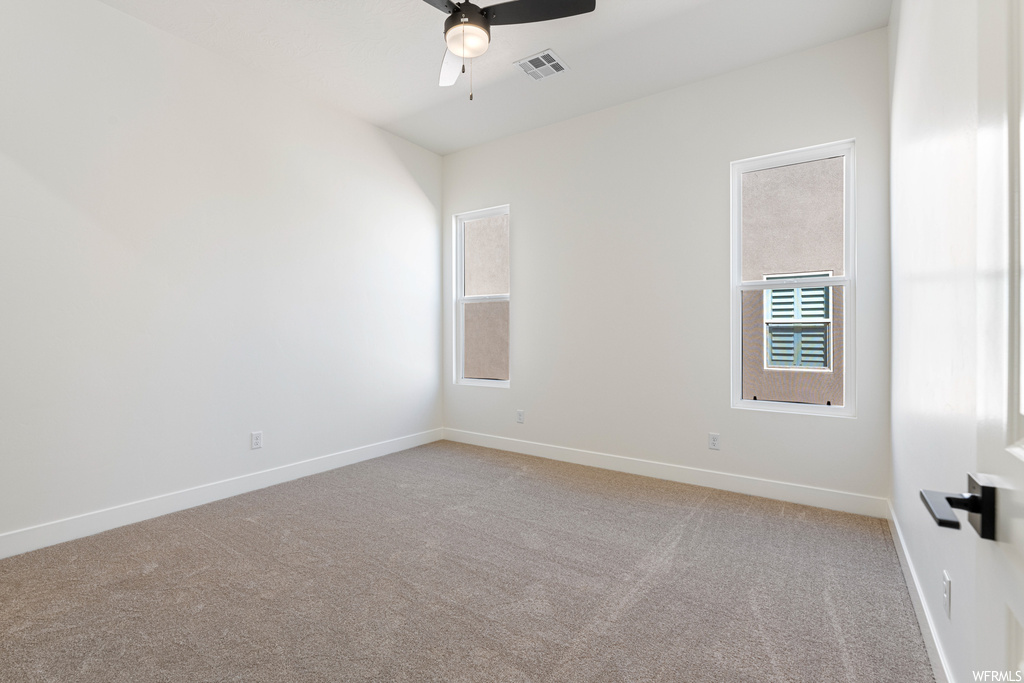 Spare room featuring light colored carpet, a healthy amount of sunlight, and ceiling fan