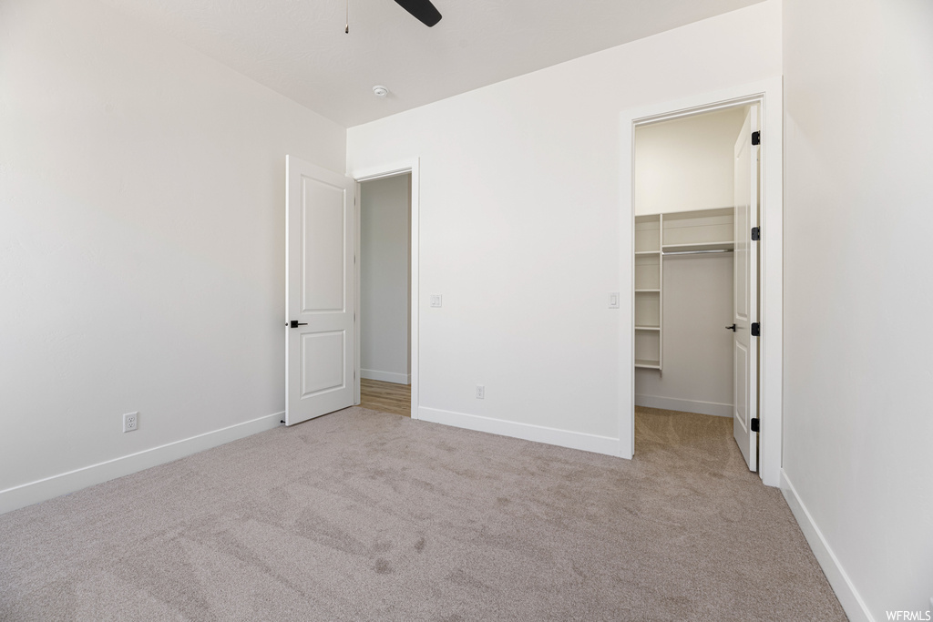 Unfurnished bedroom with a spacious closet, ceiling fan, a closet, and light colored carpet