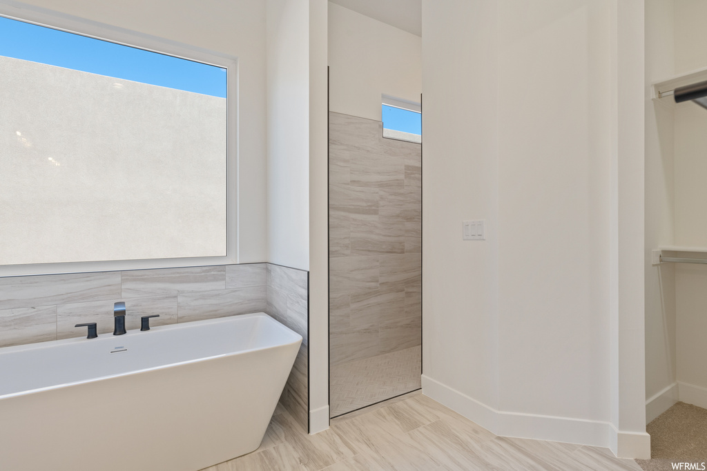 Bathroom with a bathtub, tile walls, tile flooring, and plenty of natural light