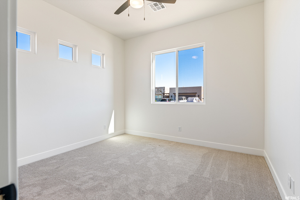 Spare room featuring ceiling fan, a wealth of natural light, and light colored carpet