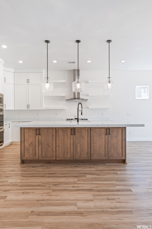 Kitchen with a center island with sink, white cabinetry, and light hardwood flooring
