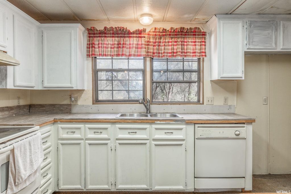 Kitchen featuring carpet, white appliances, white cabinets, and sink
