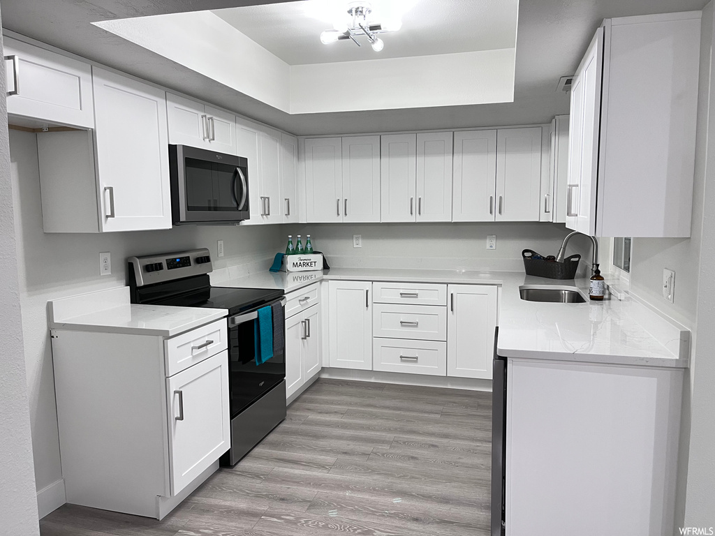 Kitchen with stainless steel appliances, white cabinetry, light hardwood flooring, and sink