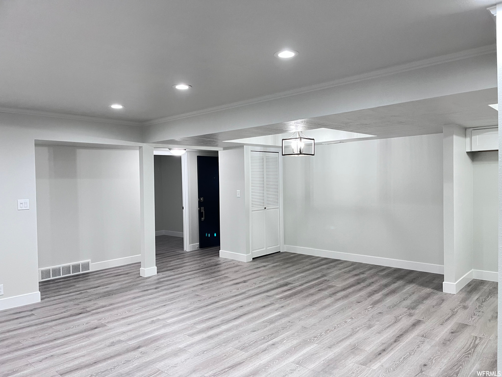 Basement featuring an inviting chandelier, light hardwood flooring, and ornamental molding