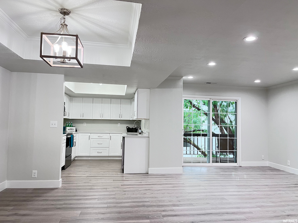 Kitchen with light hardwood floors, electric range oven, white cabinetry, pendant lighting, and a notable chandelier