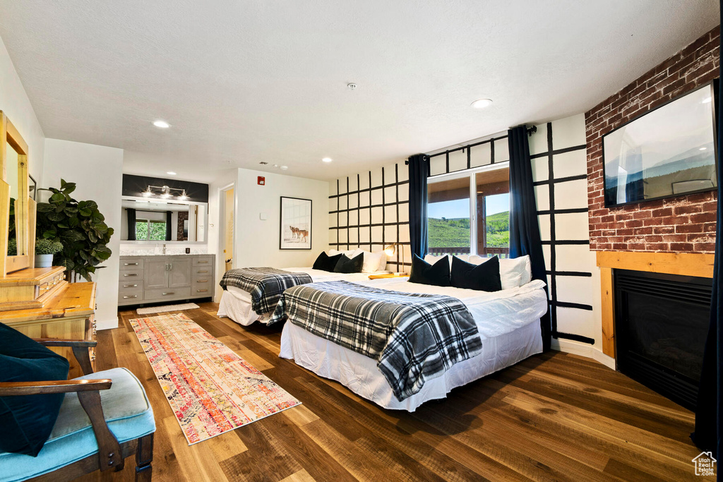 Bedroom featuring brick wall, ensuite bath, a fireplace, and dark hardwood / wood-style floors