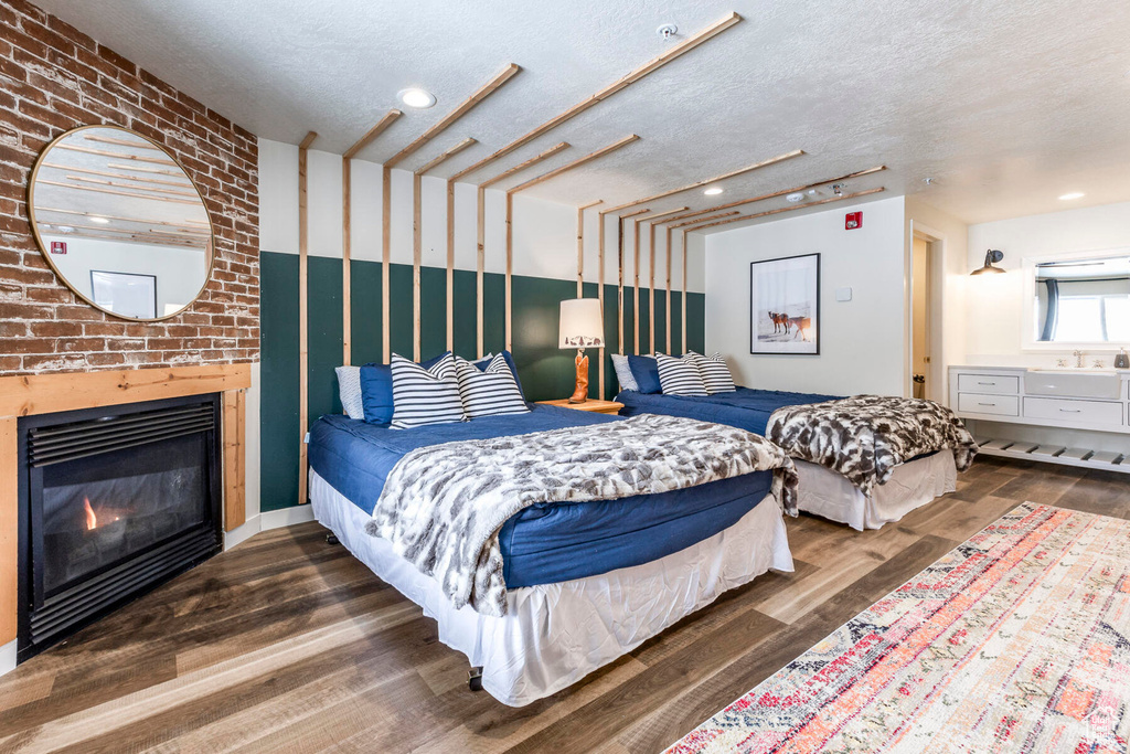 Bedroom featuring dark wood-type flooring, a textured ceiling, brick wall, and a large fireplace