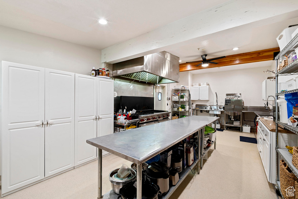 Kitchen with white cabinets, ceiling fan, wall chimney exhaust hood, and light carpet