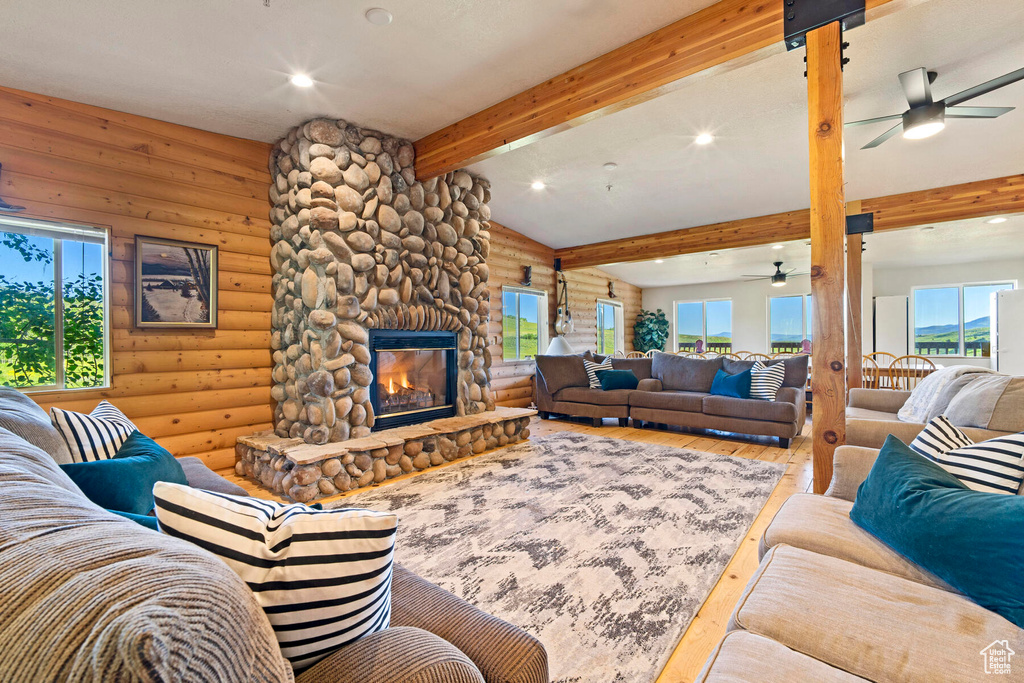 Living room with a stone fireplace, wood-type flooring, log walls, and ceiling fan