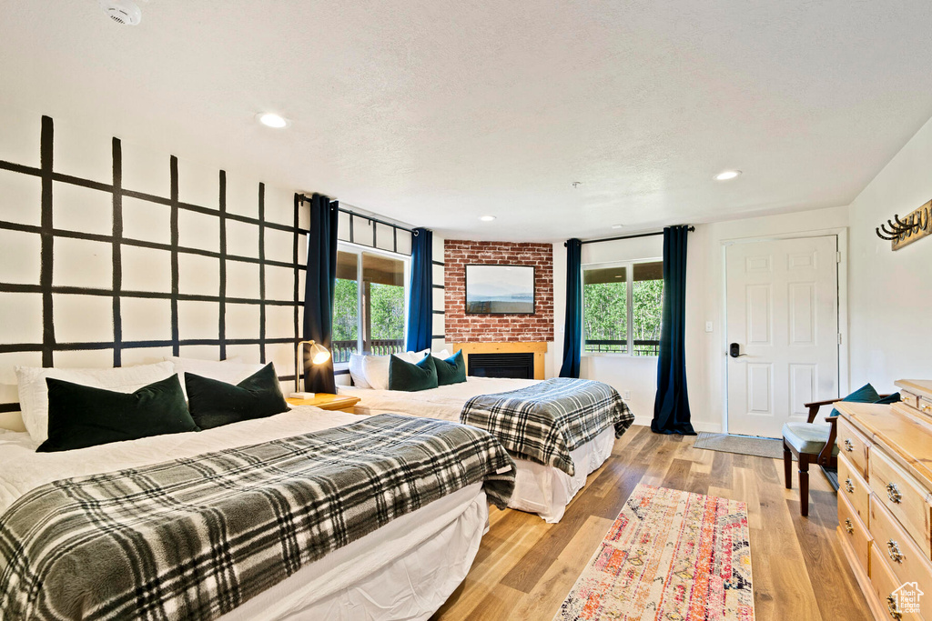Bedroom featuring multiple windows, light hardwood / wood-style floors, brick wall, and a brick fireplace