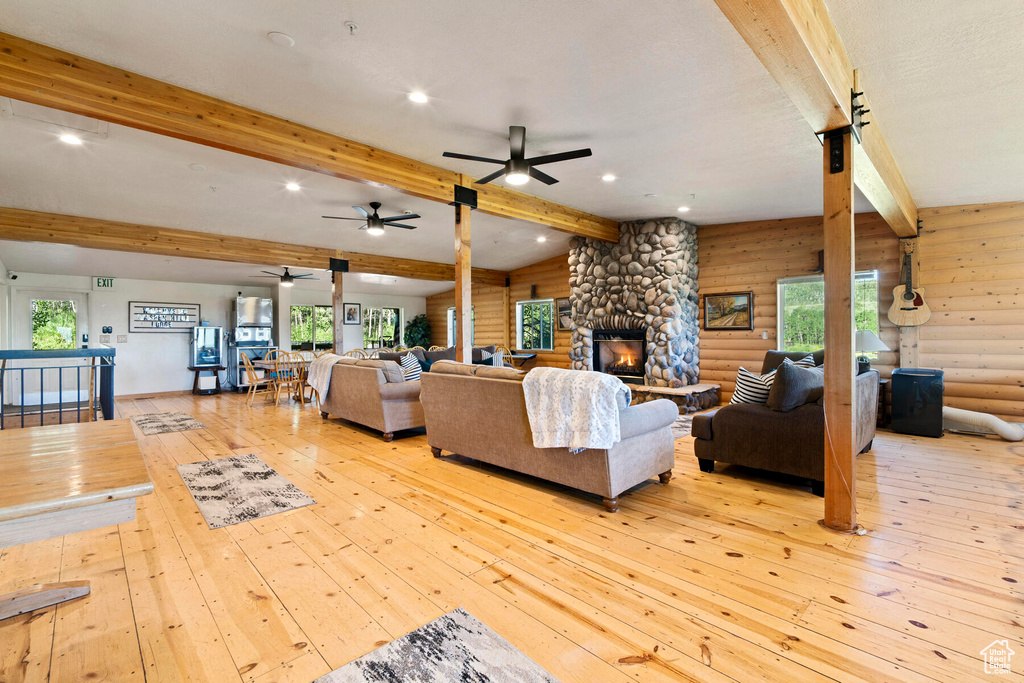 Living room featuring rustic walls, beamed ceiling, ceiling fan, and light hardwood / wood-style floors