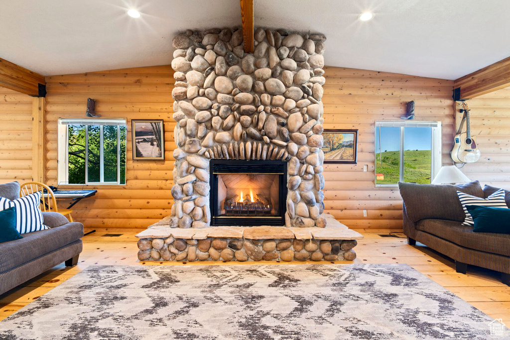 Living room with a fireplace, wood-type flooring, rustic walls, and vaulted ceiling with beams