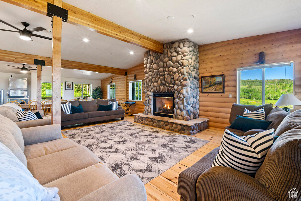 Living room featuring a stone fireplace, light hardwood / wood-style flooring, lofted ceiling with beams, and ceiling fan
