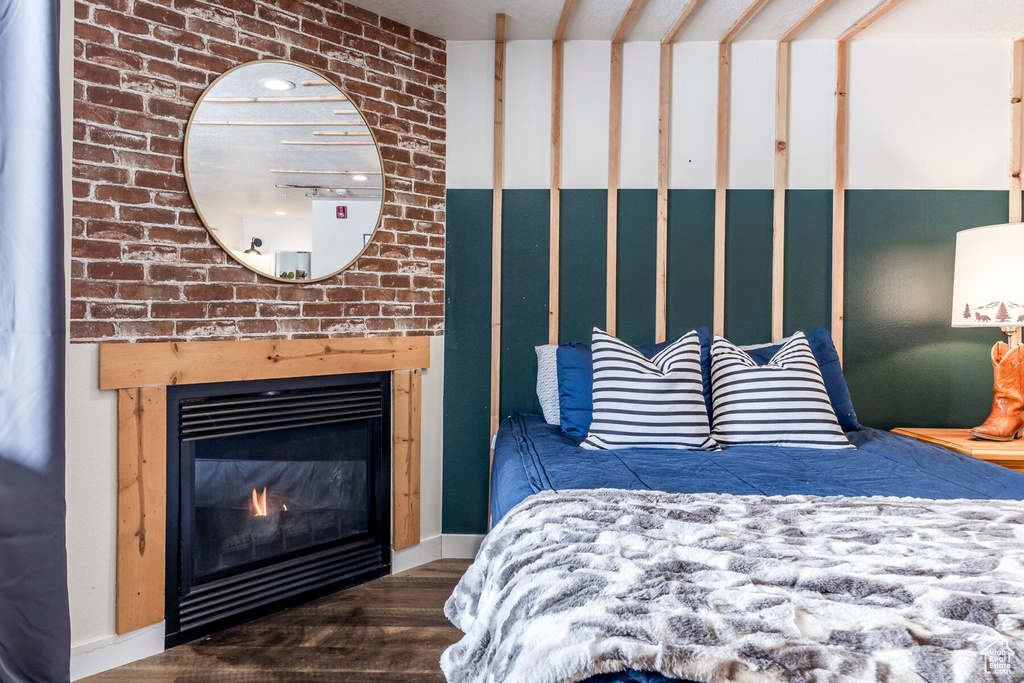 Bedroom featuring a brick fireplace, dark hardwood / wood-style flooring, and brick wall
