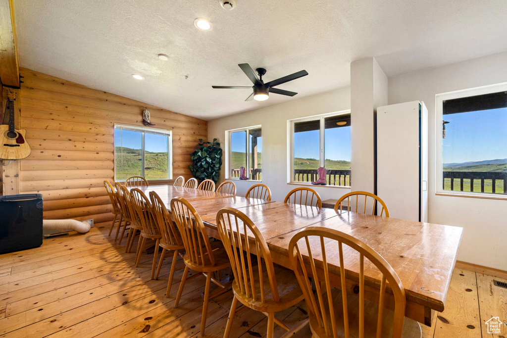 Dining room with ceiling fan, a textured ceiling, log walls, light hardwood / wood-style flooring, and vaulted ceiling