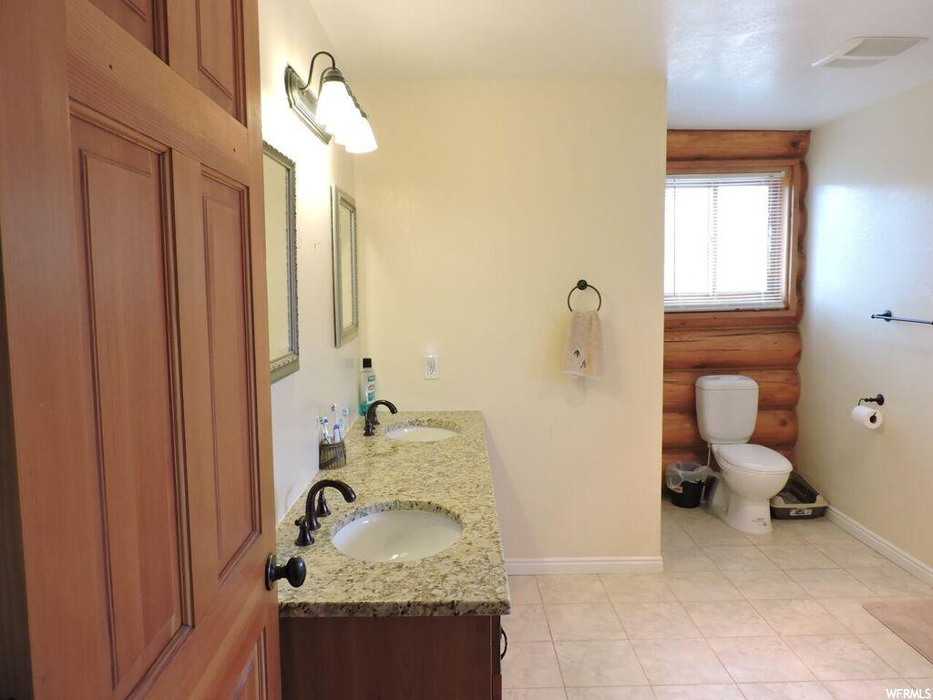 Bathroom with double sink vanity, tile floors, and toilet