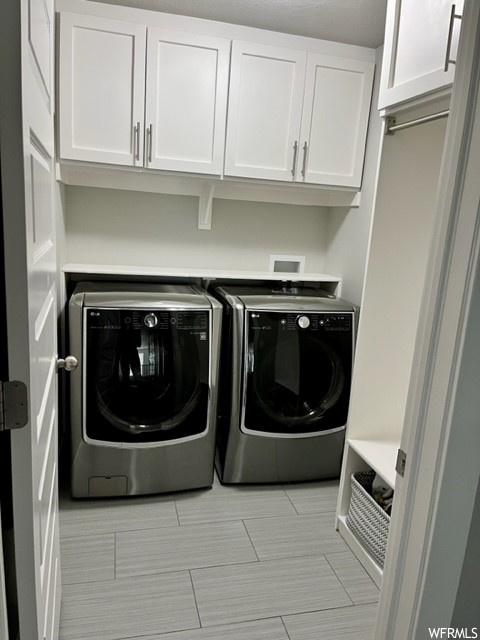 Washroom with washing machine and clothes dryer, light tile floors, cabinets, and washer hookup