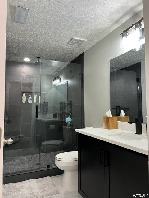Bathroom with a shower with door, toilet, vanity, and a textured ceiling