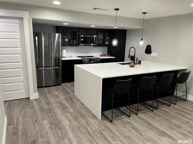 Kitchen featuring sink, light hardwood flooring, hanging light fixtures, tasteful backsplash, and appliances with stainless steel finishes