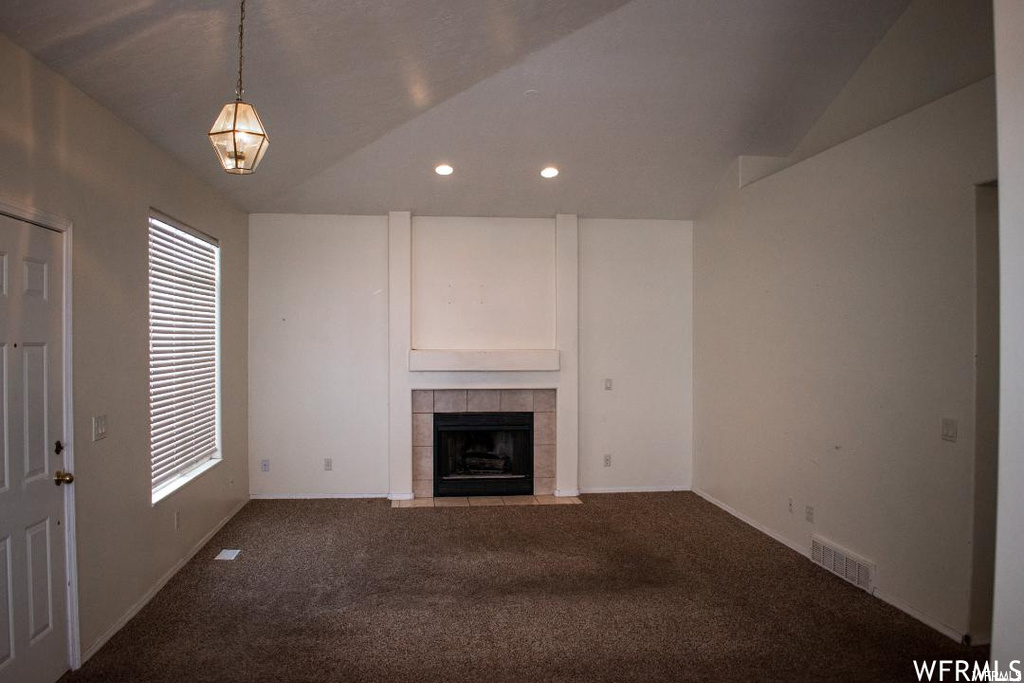 Unfurnished living room with lofted ceiling, dark carpet, and a fireplace