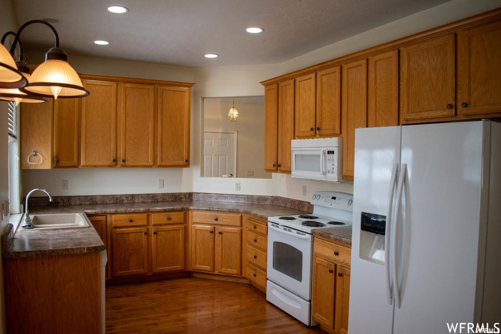 Kitchen featuring white appliances, sink, dark hardwood floors, and pendant lighting