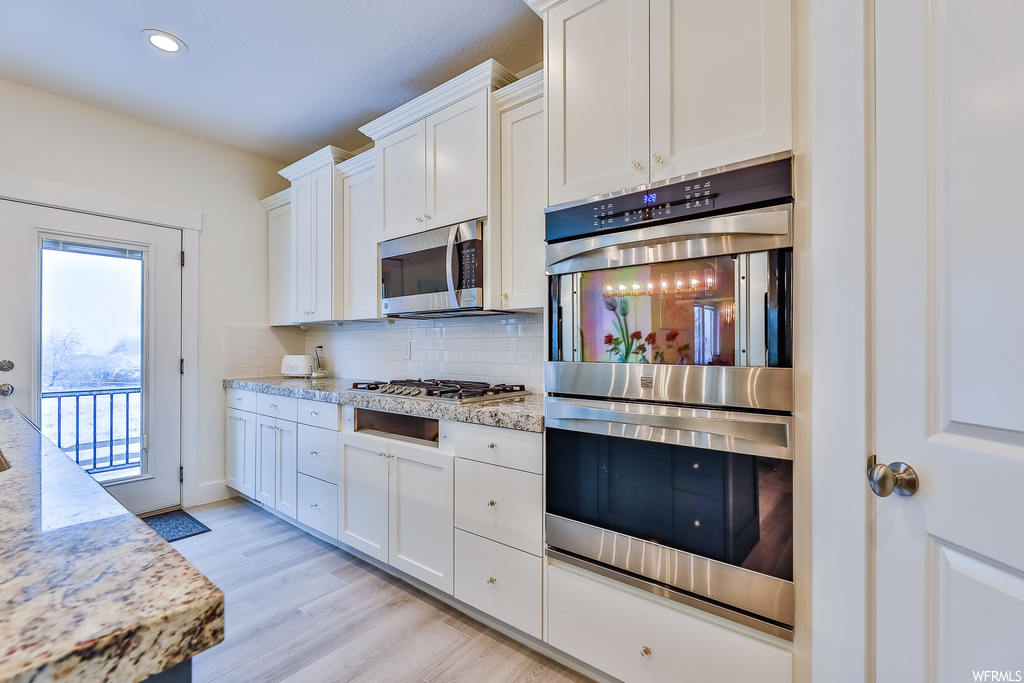 Kitchen featuring white cabinets, backsplash, stainless steel appliances, and light hardwood floors
