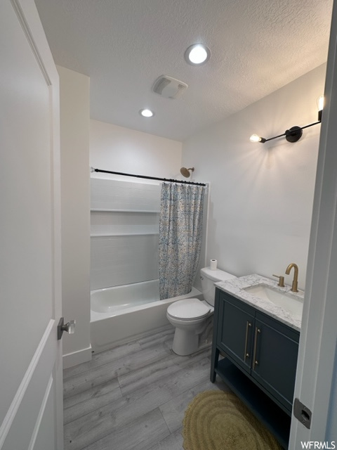 Full bathroom featuring toilet, shower / tub combo with curtain, a textured ceiling, hardwood floors, and vanity