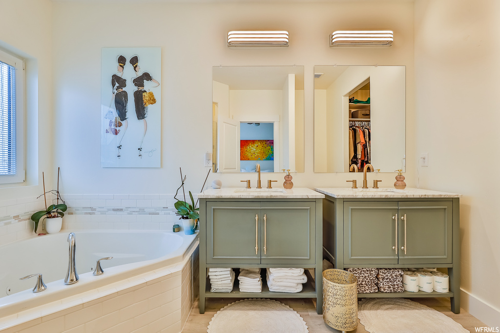 Bathroom featuring tiled bath, tile floors, and dual vanity