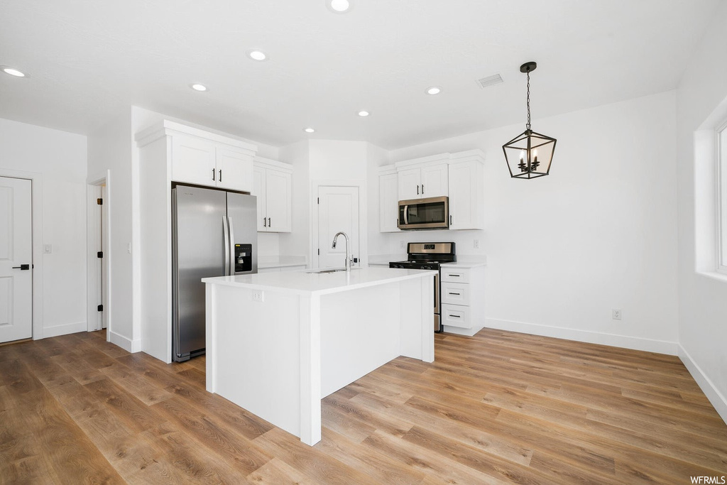 Kitchen featuring appliances with stainless steel finishes, white cabinetry, pendant lighting, light countertops, and light hardwood flooring