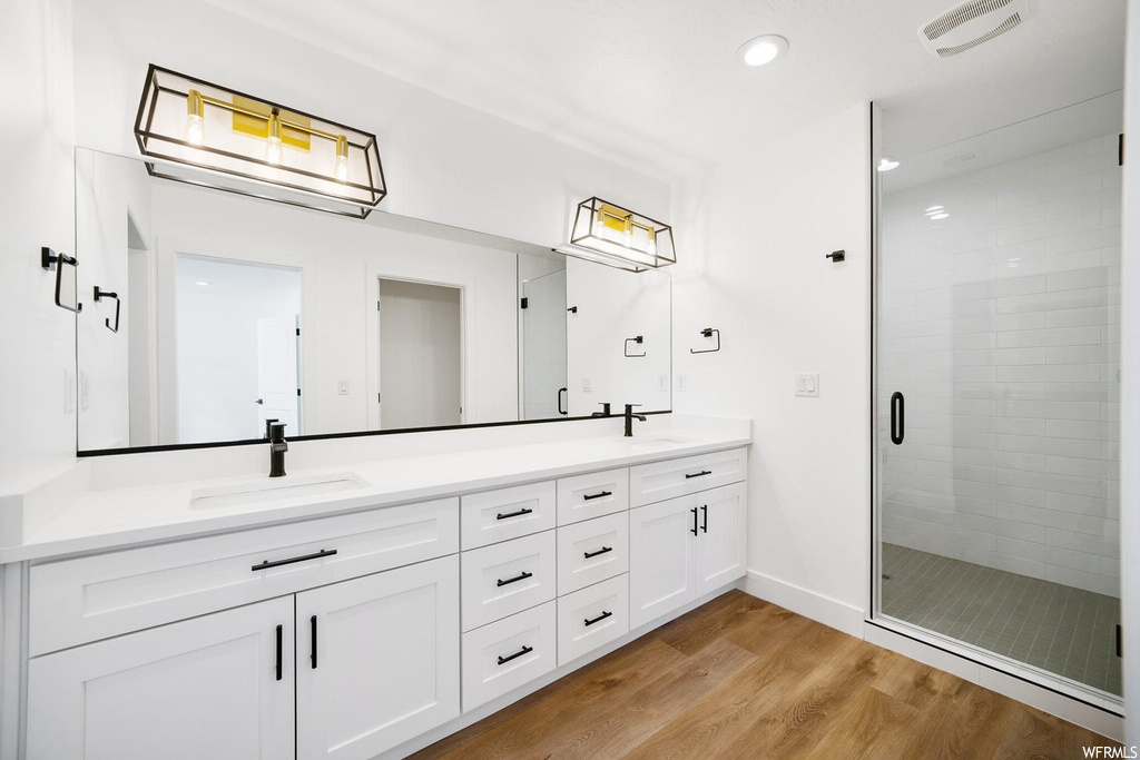 Bathroom featuring a shower with shower door, mirror, double sink vanity, and light hardwood floors