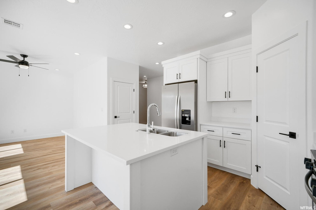 Kitchen featuring kitchen island with sink, light countertops, white cabinetry, light hardwood flooring, ceiling fan, and stainless steel fridge with ice dispenser