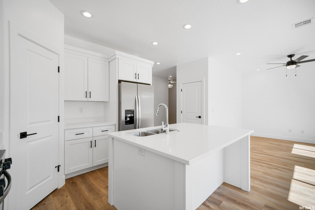 Kitchen featuring white cabinets, light countertops, light hardwood flooring, kitchen island with sink, stainless steel fridge with ice dispenser, and ceiling fan