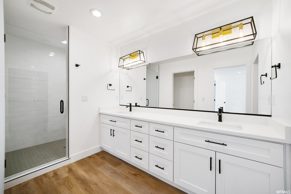 Bathroom with an enclosed shower, double vanity, mirror, and light hardwood flooring