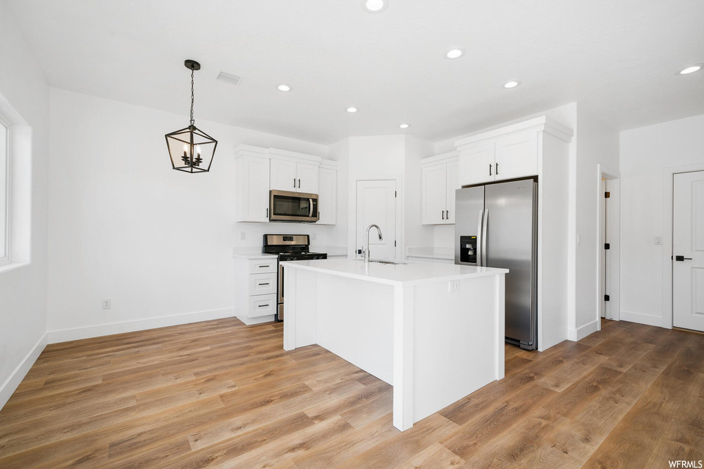 Kitchen featuring light hardwood flooring, stainless steel appliances, light countertops, and white cabinets