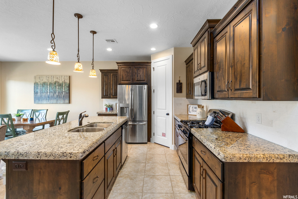 Kitchen featuring sink, pendant lighting, an island with sink, light tile flooring, and appliances with stainless steel finishes