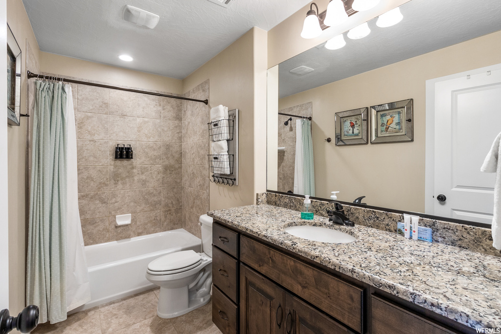 Full bathroom featuring toilet, a textured ceiling, tile floors, vanity with extensive cabinet space, and shower / tub combo