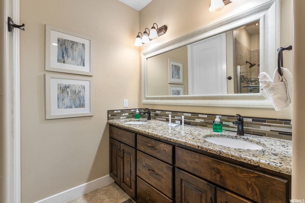 Bathroom with double sink, tile flooring, tasteful backsplash, and vanity with extensive cabinet space