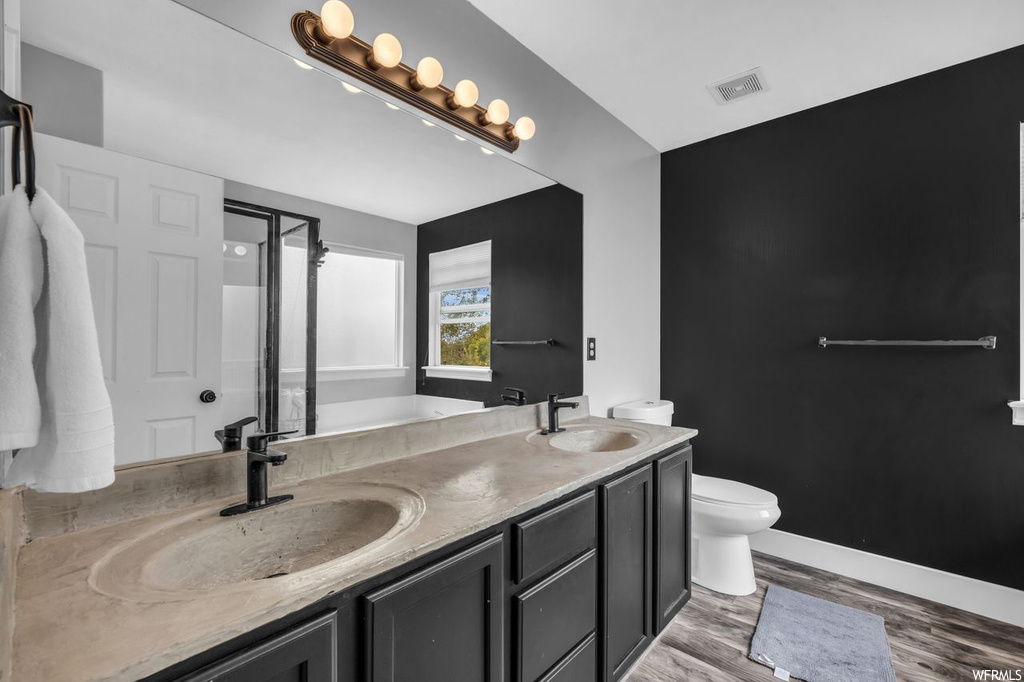 Bathroom featuring hardwood flooring, large vanity, toilet, and dual sinks