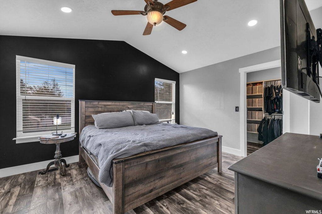 Hardwood floored bedroom featuring a walk in closet, vaulted ceiling, a closet, and ceiling fan