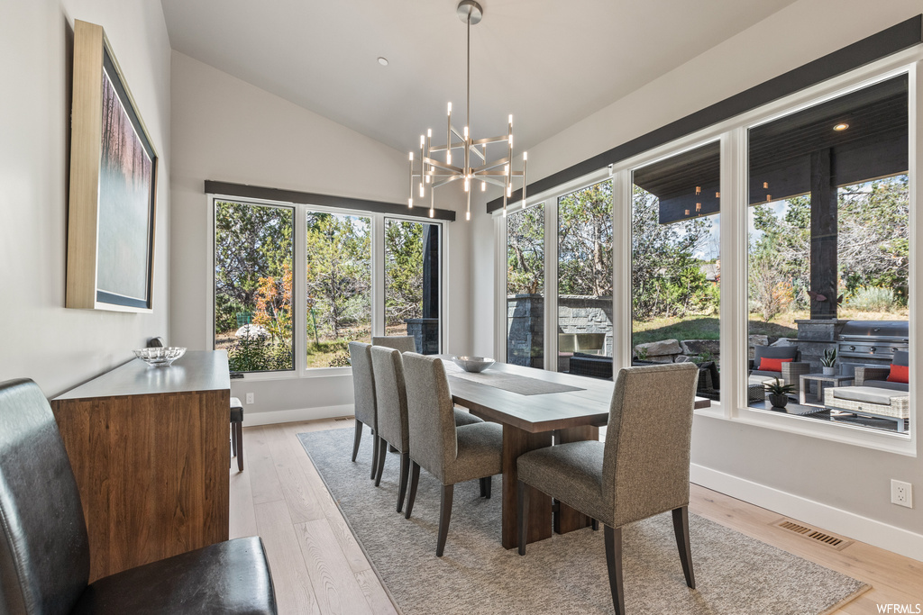 Hardwood floored dining space with a notable chandelier and vaulted ceiling