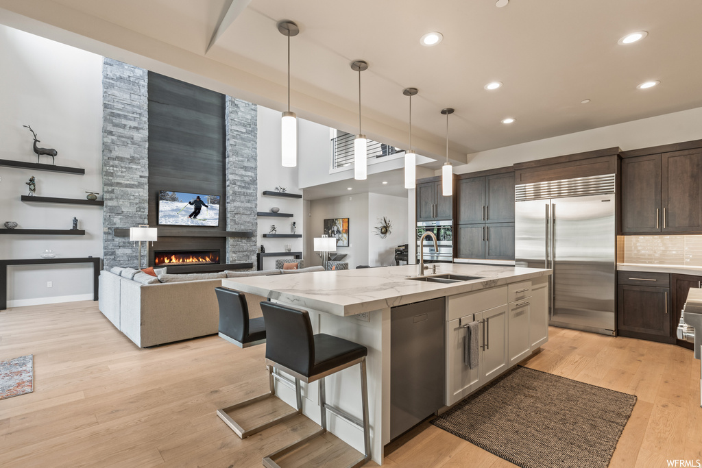 Kitchen featuring stainless steel appliances, decorative light fixtures, a fireplace, light countertops, backsplash, light hardwood floors, and a high ceiling