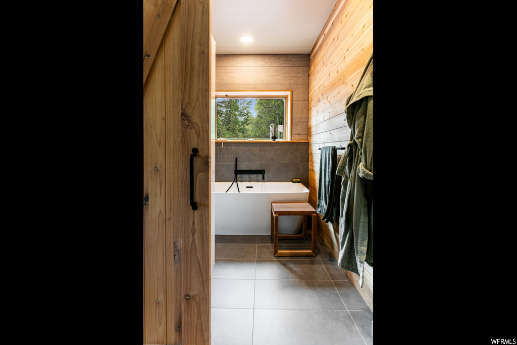 Bathroom featuring wooden walls, a bathing tub, and light tile floors