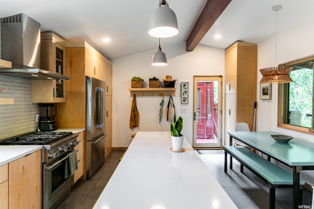 Kitchen featuring dark tile floors, appliances with stainless steel finishes, decorative light fixtures, wall chimney exhaust hood, lofted ceiling with beams, and backsplash