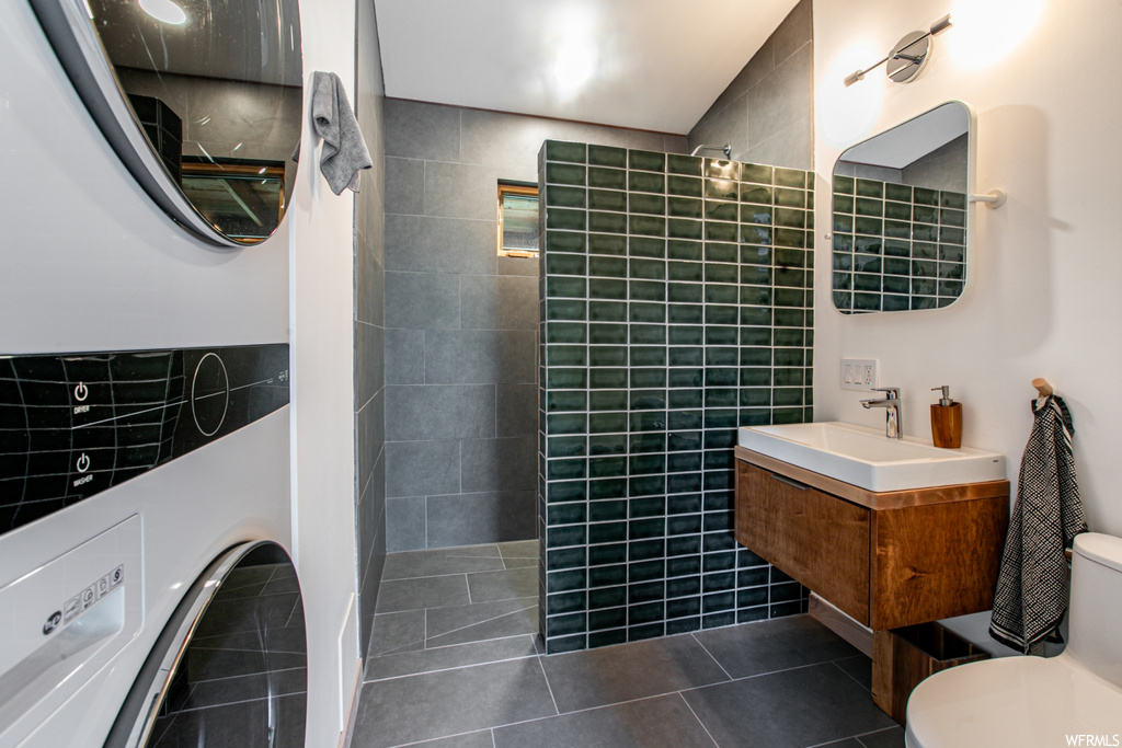 Bathroom featuring tiled shower, mirror, dark tile floors, large vanity, and tile walls
